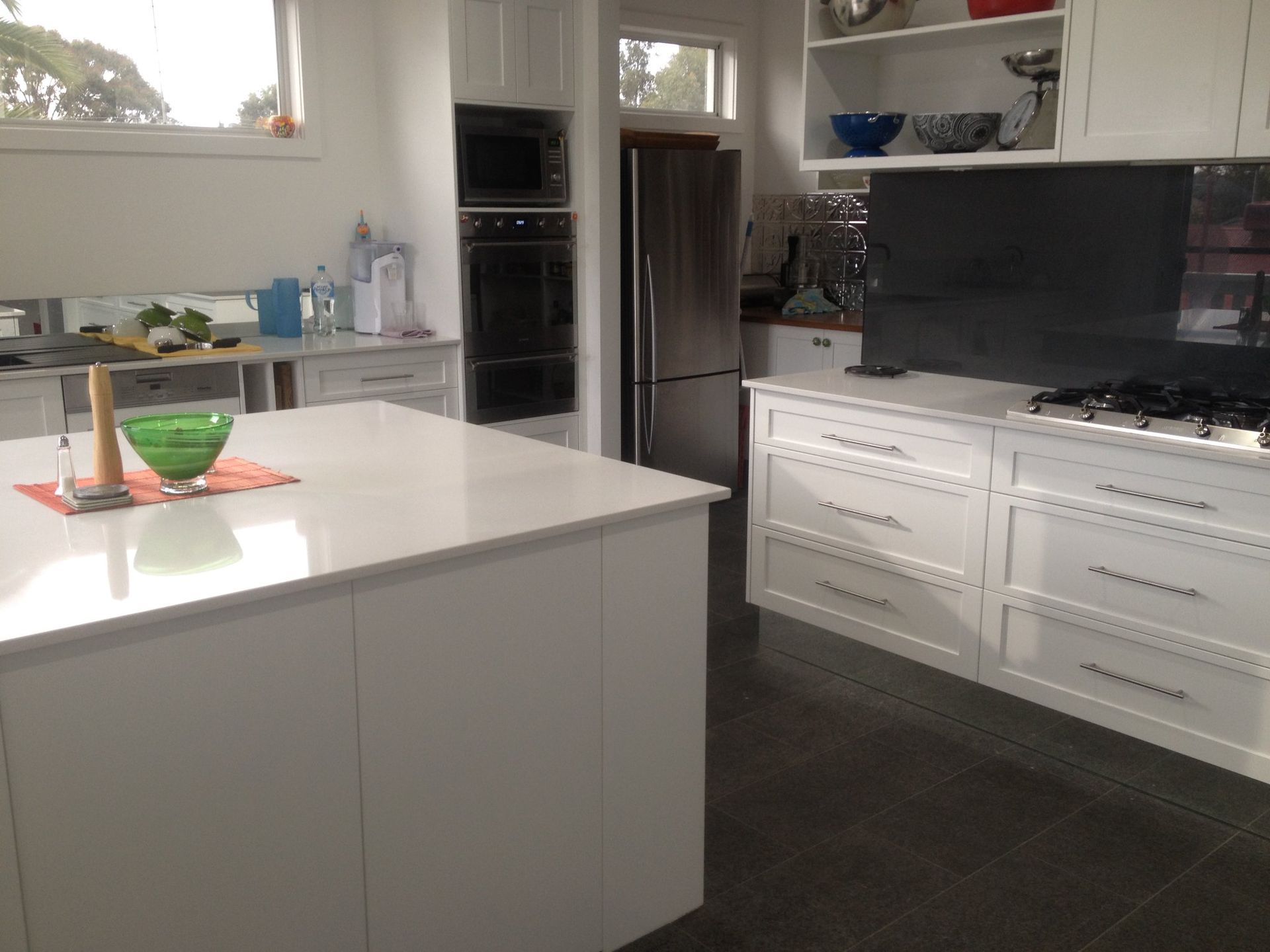 White kitchen with island, cabinets, oven, and refrigerator. Dark tiled floor.