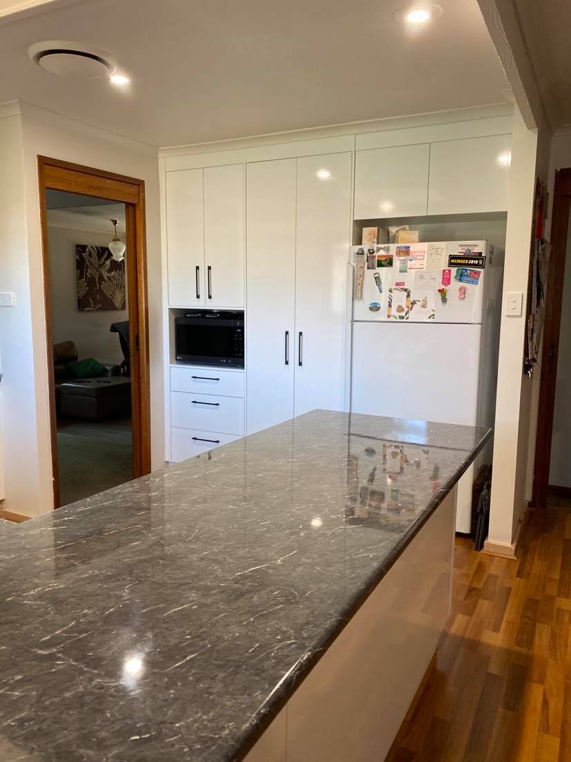 Kitchen with white cabinets, dark countertop island, and refrigerator; doorway to another room.