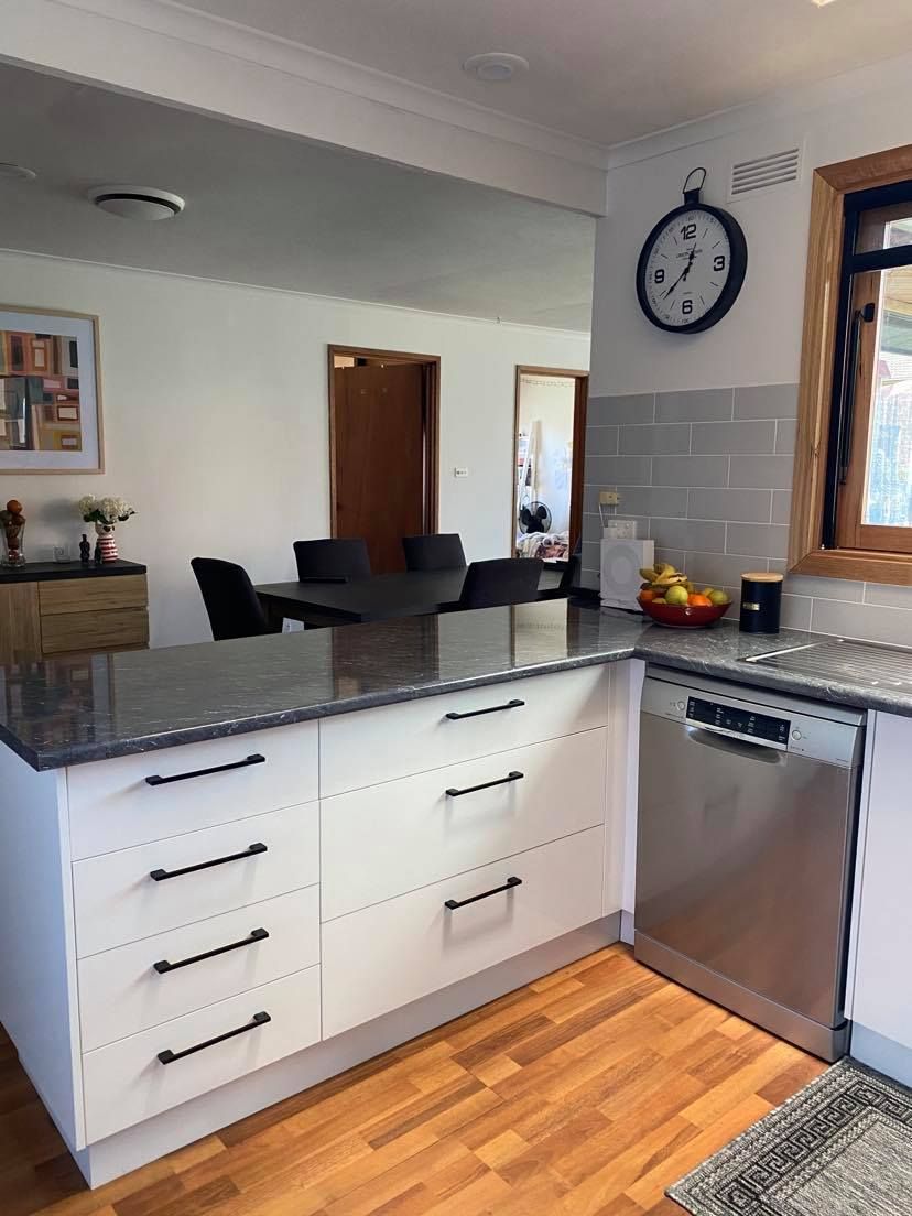 Kitchen with white cabinets, gray countertop, stainless steel dishwasher, and a clock.