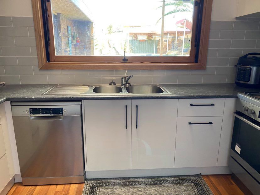 Kitchen with stainless steel dishwasher, sink, white cabinets, and a window.