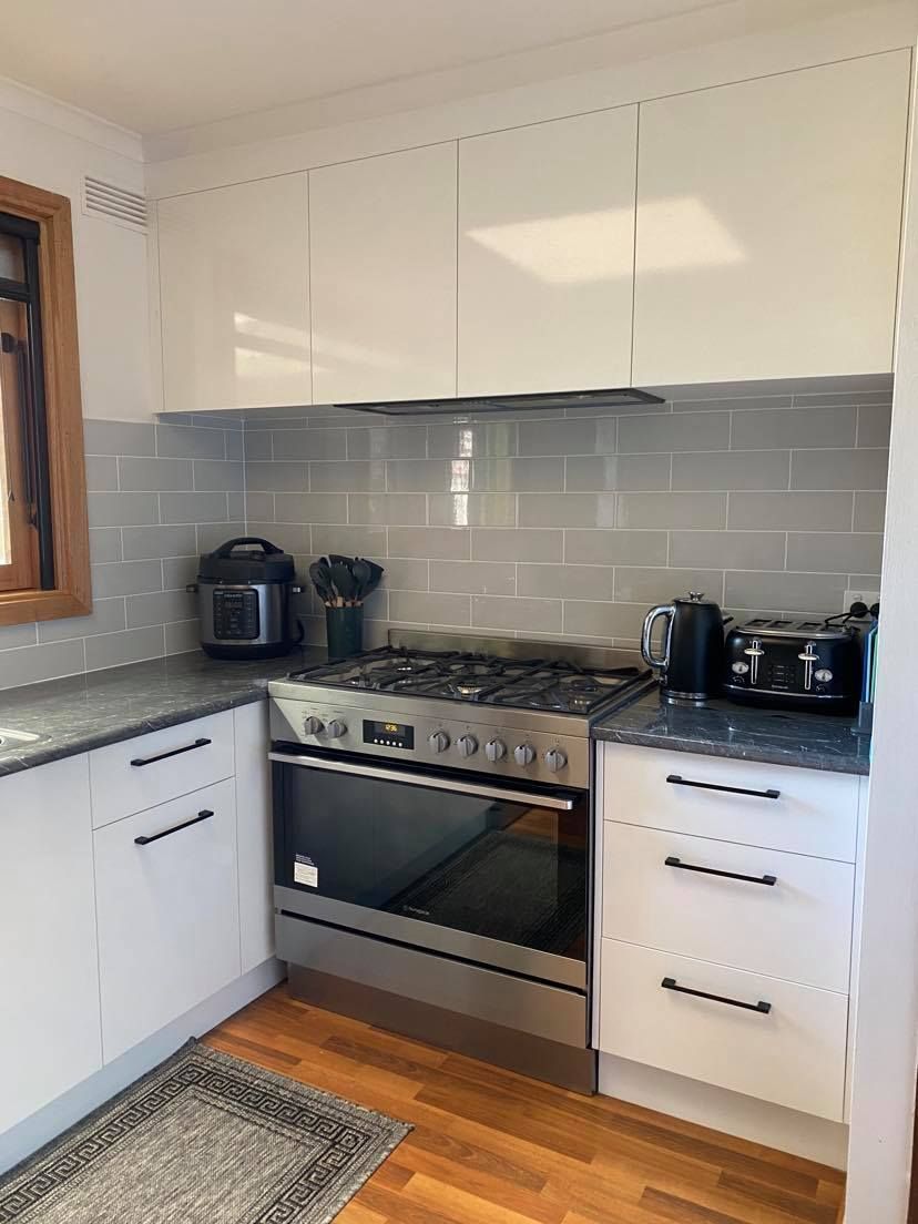 Kitchen with white cabinets, gray backsplash, stainless steel stove, and wooden floor.