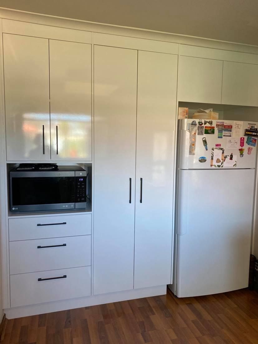 White kitchen cabinets with a built-in microwave, drawers, and a refrigerator.