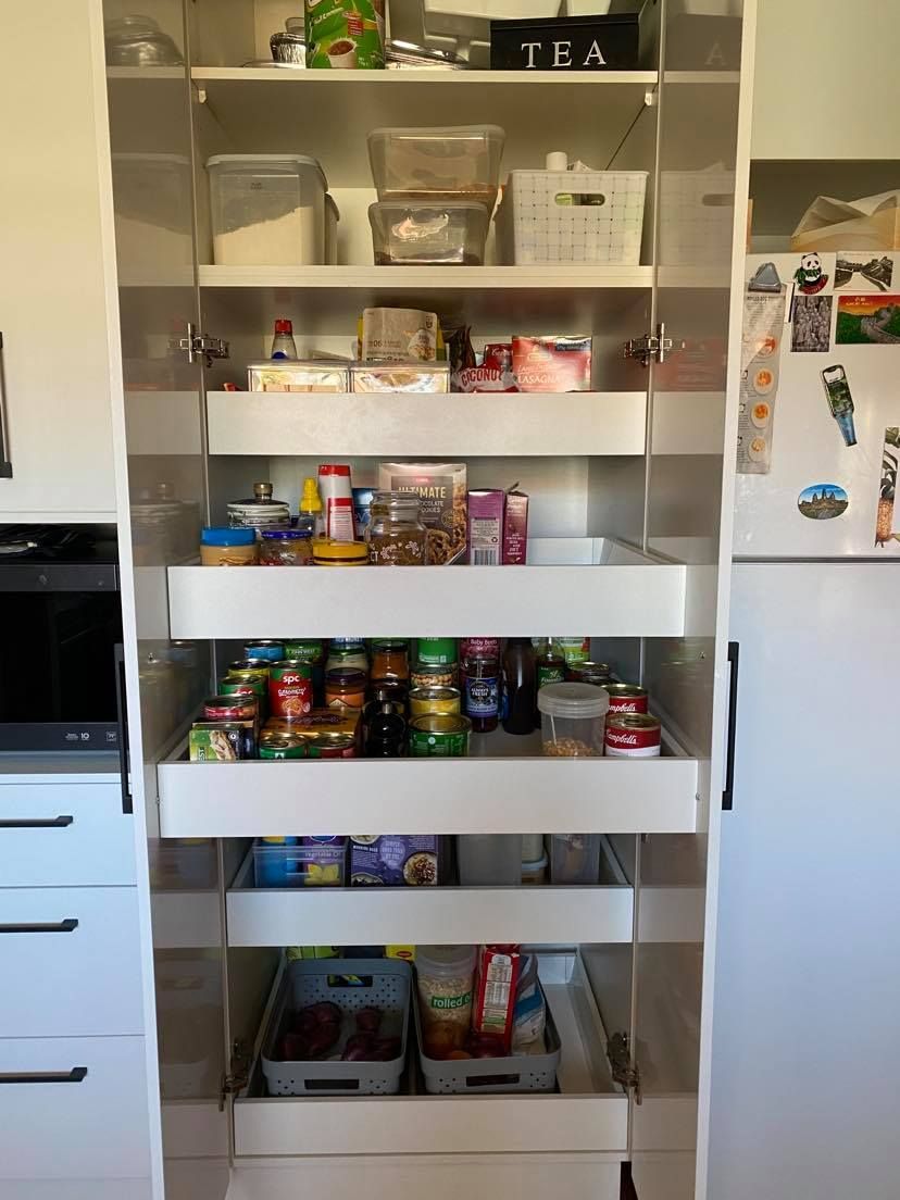 White pantry cabinet with pull-out drawers filled with various food items; kitchen setting.