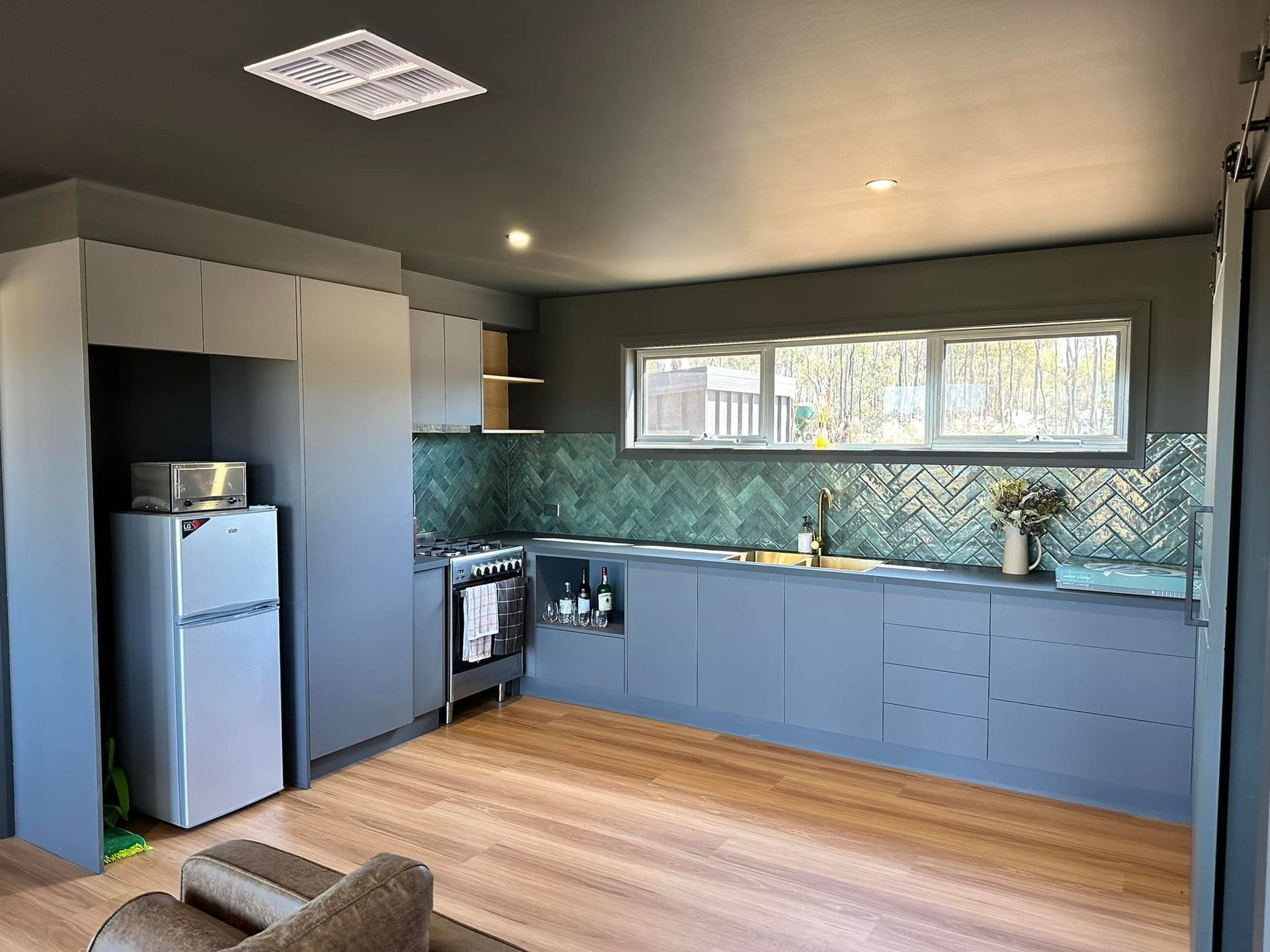 Gray kitchen with wood floor, teal backsplash, and stainless steel appliances.