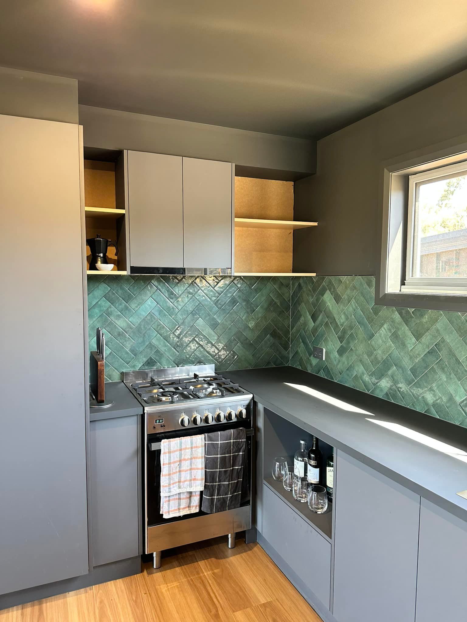Gray kitchen with green tile backsplash, stainless steel stove, and small window.