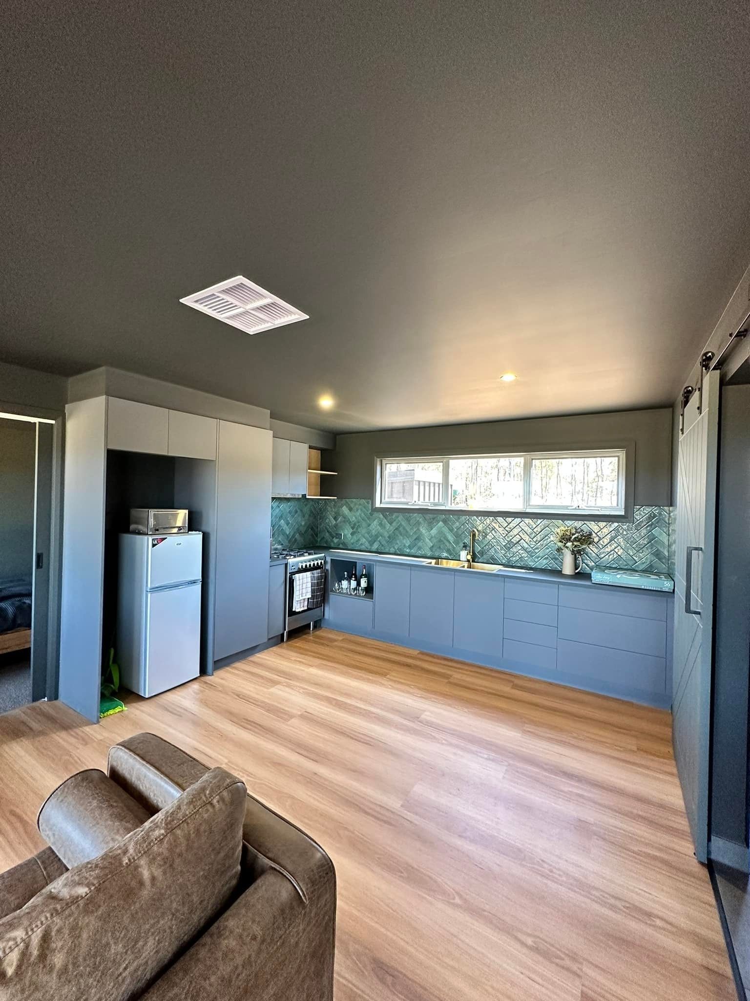 Kitchen interior with grey cabinetry, teal backsplash, refrigerator, and wooden floors.