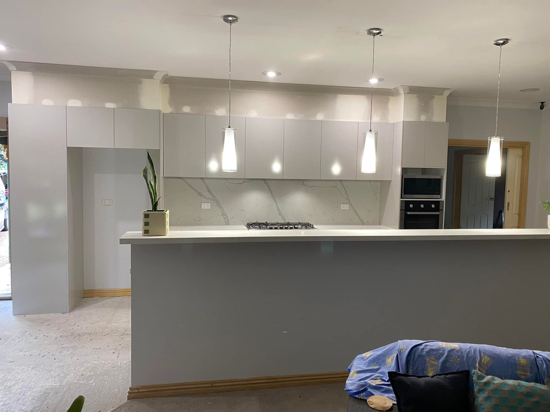 Modern kitchen with white cabinets, countertop, and pendant lights. A light-colored stone backsplash and gray island.