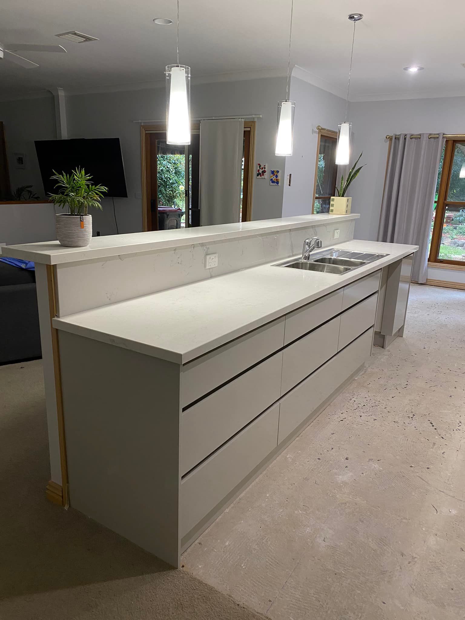 Light gray kitchen island with drawers, sink, and pendant lights.