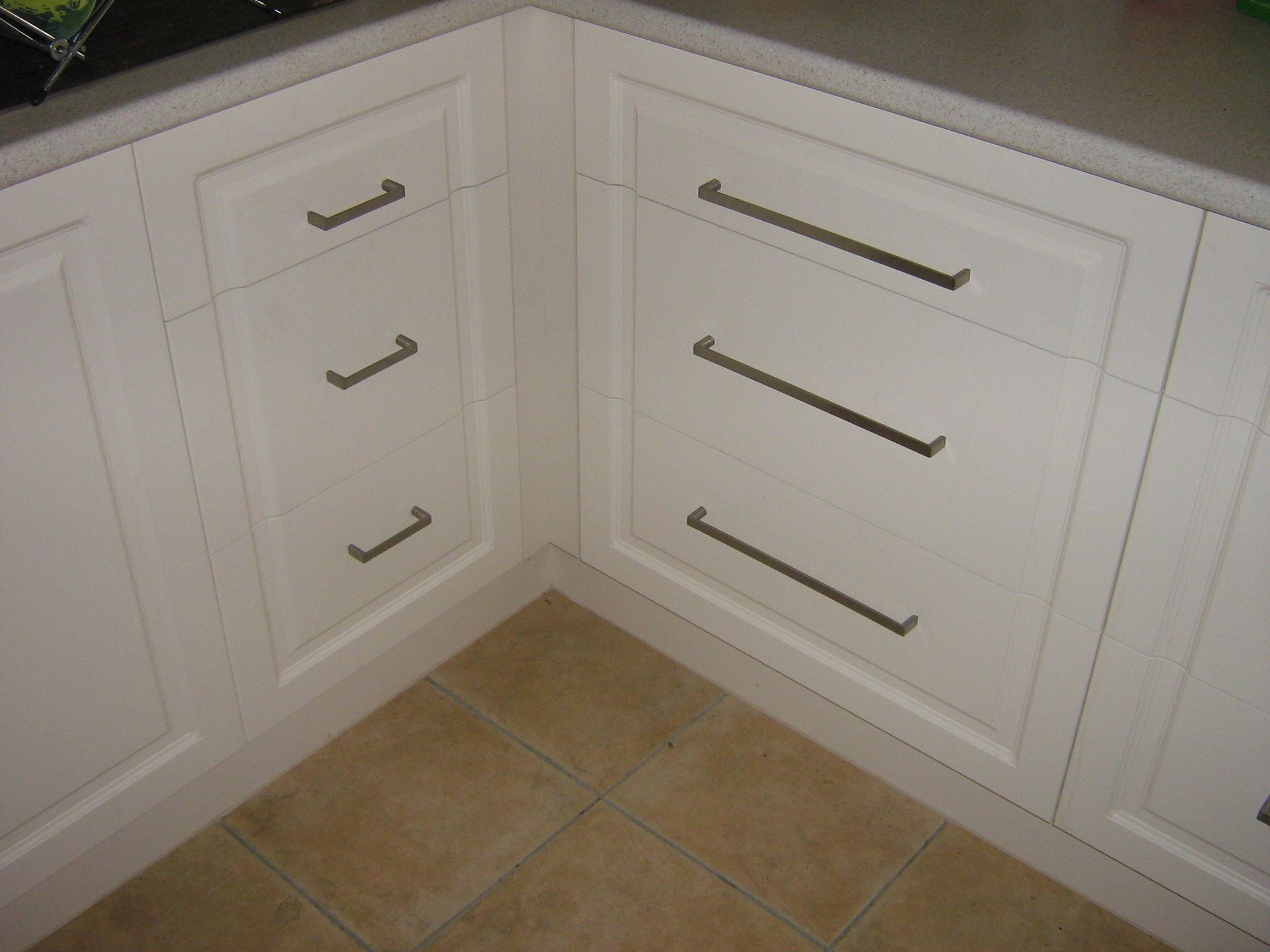 White kitchen cabinets with gray countertops and drawers with long, dark pulls.