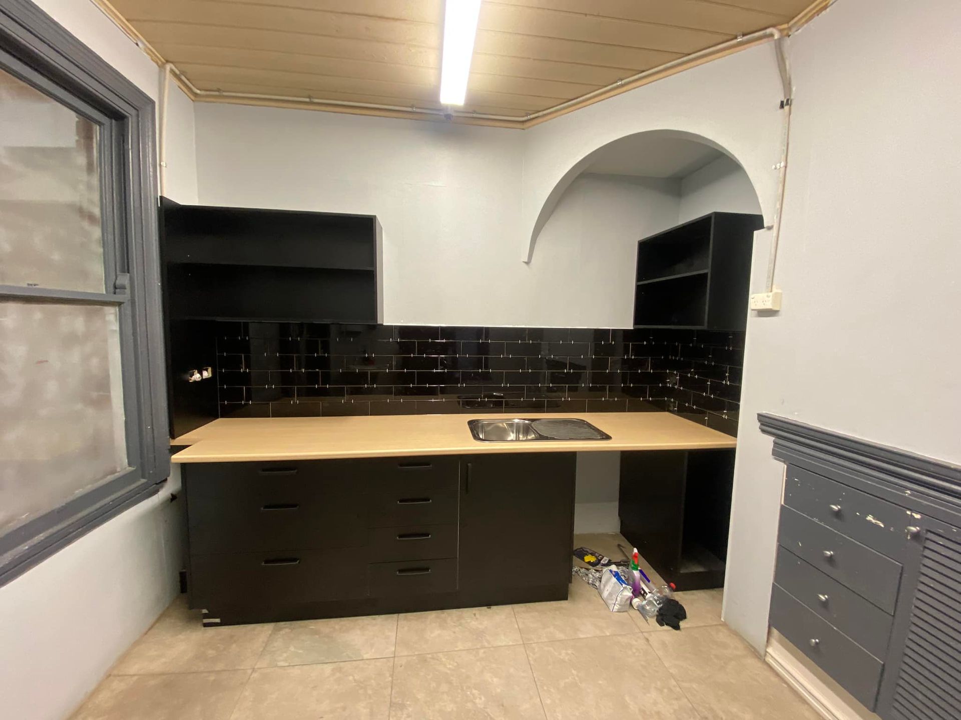 Black kitchen cabinets and backsplash in a small room with light-colored countertops and walls.