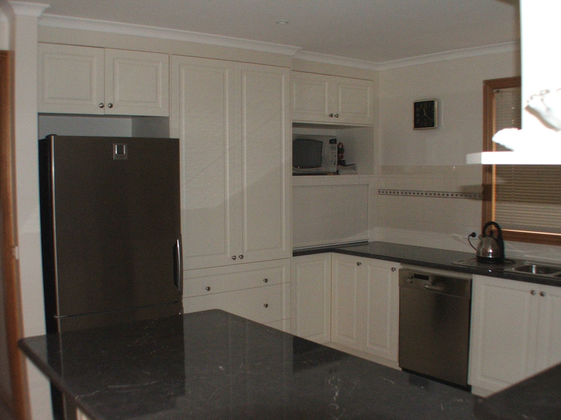 White kitchen cabinets, black countertop, stainless steel appliances, and a microwave.
