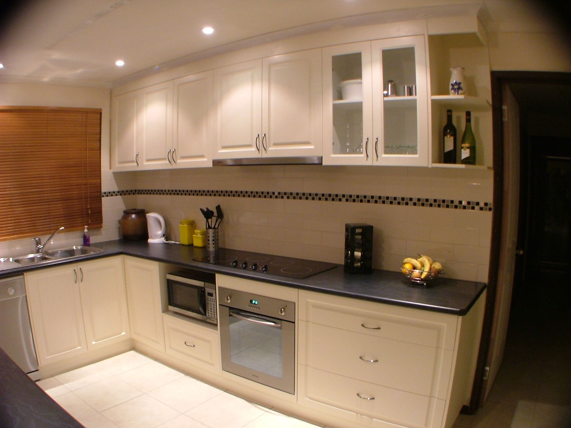 Cream-colored kitchen cabinets with appliances, dark countertop, and tiled backsplash.