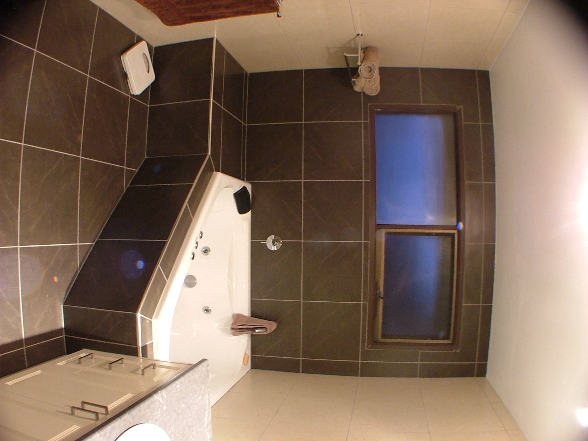 Bathroom with brown tiled walls, white jacuzzi tub, and a window.