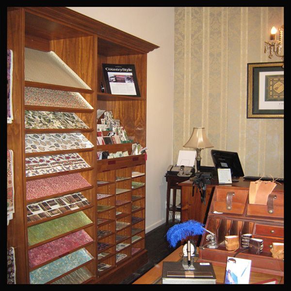 Wooden display cabinet with samples, desk with computer, and wallpaper in a store.