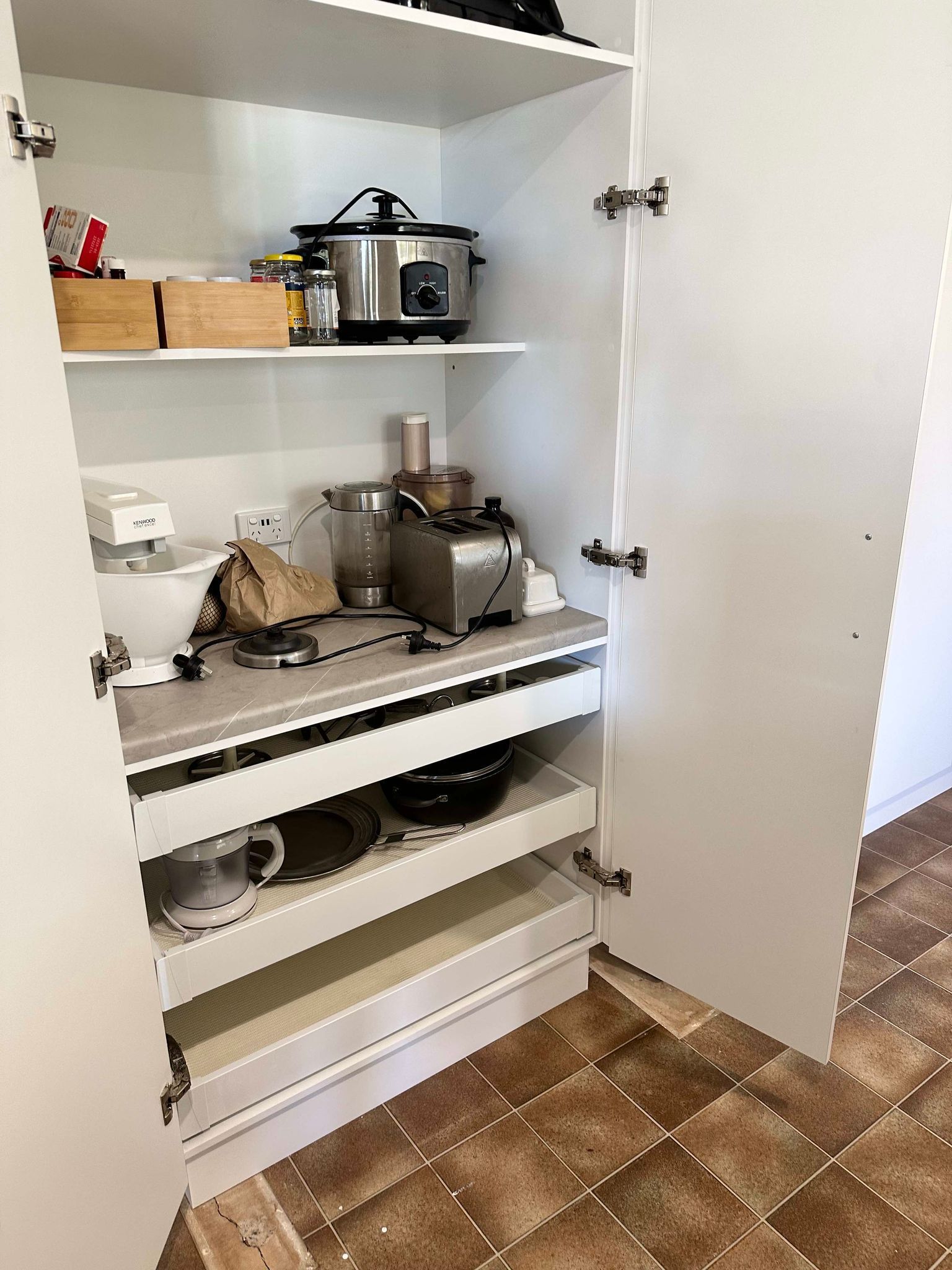 White pantry with open doors, containing kitchen appliances and pull-out shelves.