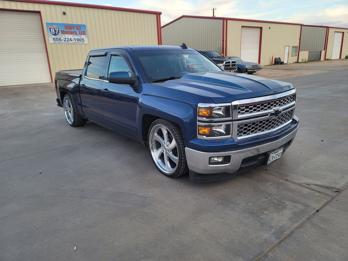 Blue pickup truck parked in an industrial lot beside beige storage buildings.