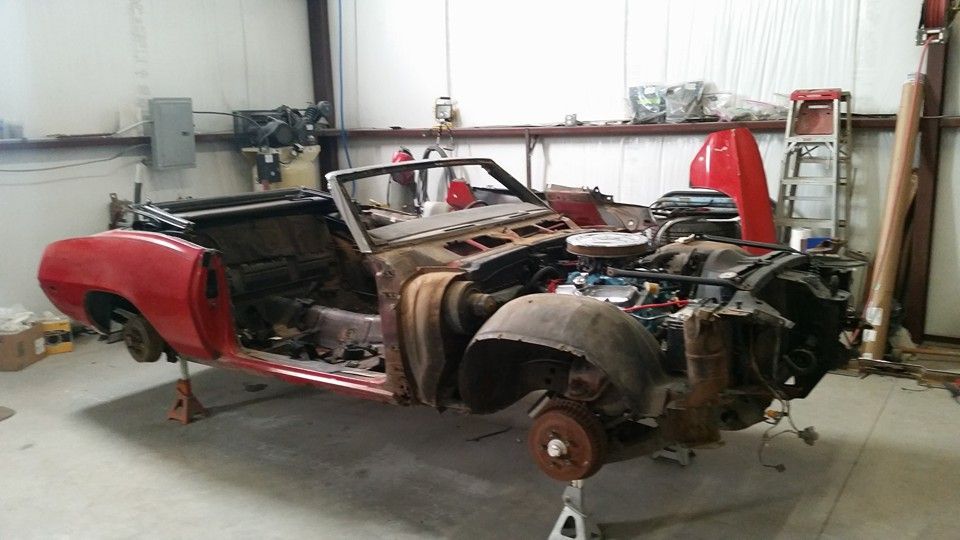 Partially restored red vintage car body in a workshop, missing wheels and engine parts.