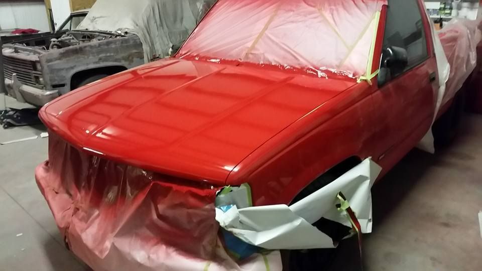 Red car in a body shop, masked with plastic and partially painted bright red.