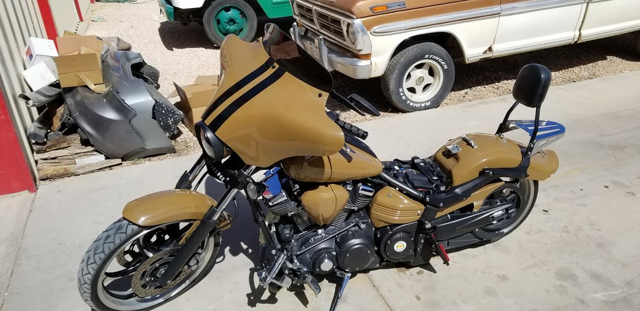 Tan-and-black custom motorcycle parked outdoors beside a white pickup truck.