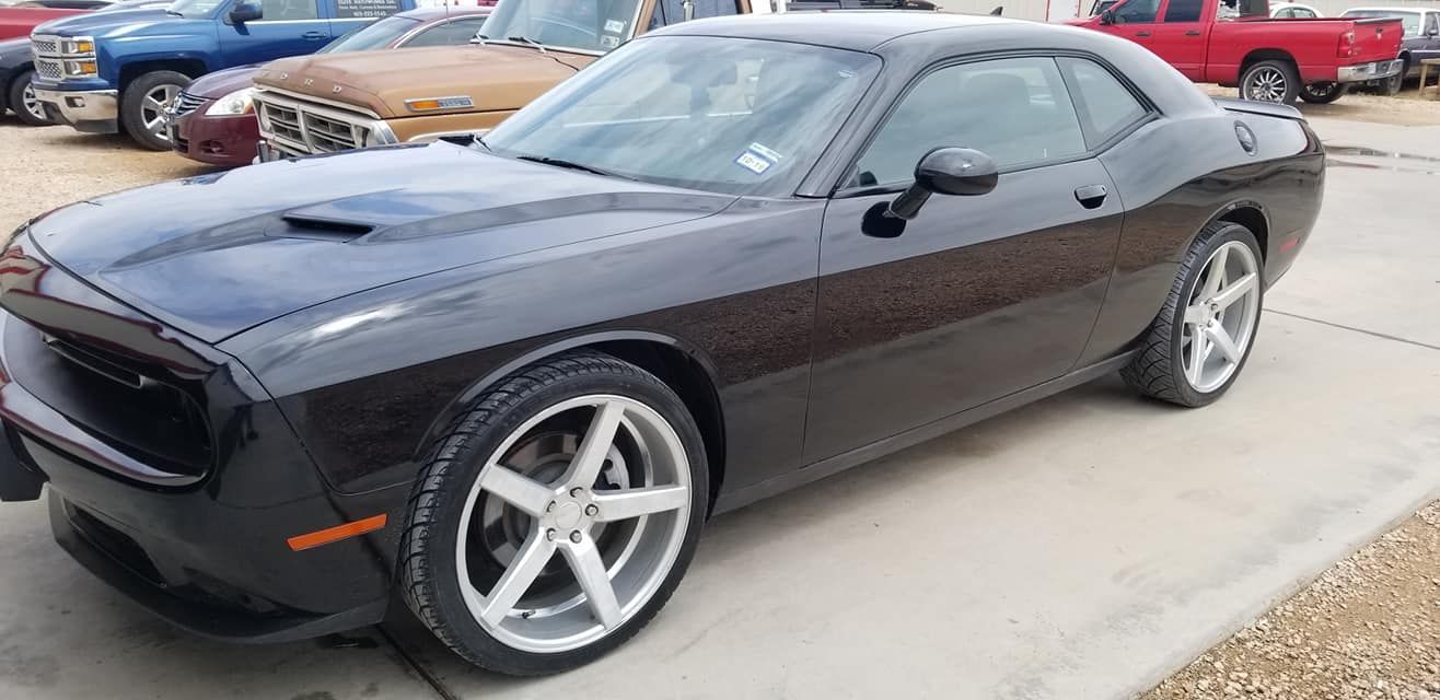Black Dodge Challenger parked outdoors, side view with silver rims and hood scoop