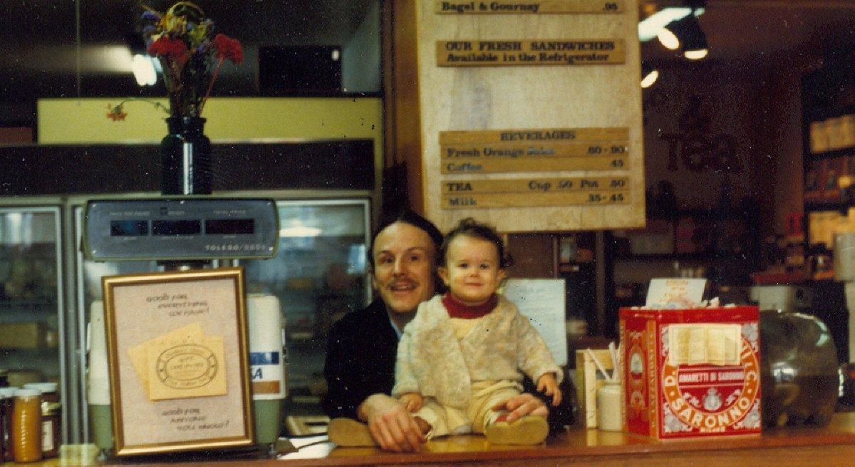 Person and child at a bakery counter with framed awards and pastry displays behind them.