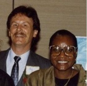 Two people smiling at a formal event, wearing suits and glasses.