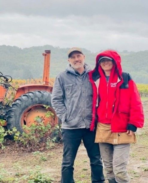 Two people in rain gear standing beside an old tractor in a misty field