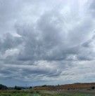 Cloudy sky over a grassy landscape with a distant horizon and low hills