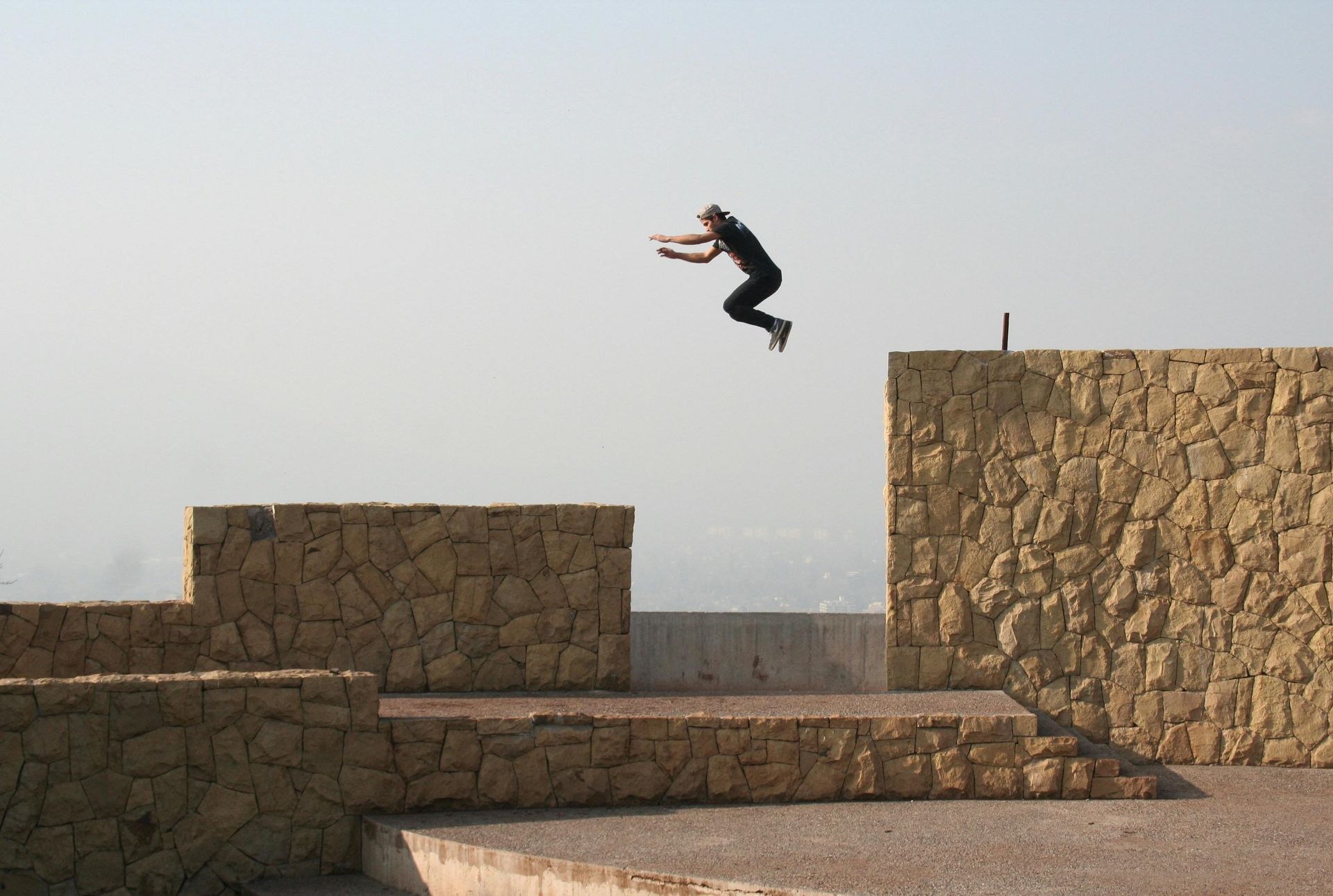 Person mid-jump between stone walls in a sunny outdoor setting