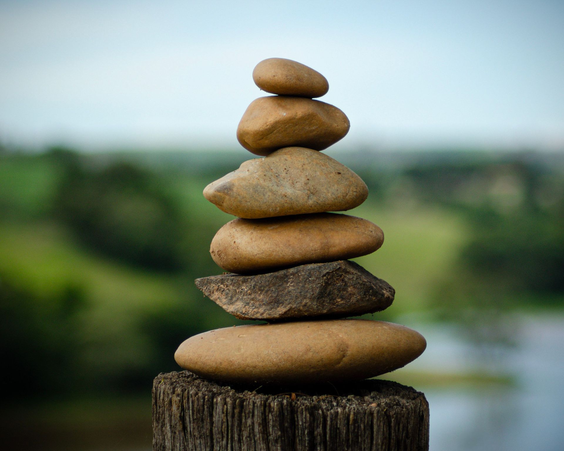 Stacked smooth stones balanced on a wooden post with a blurred green landscape behind.