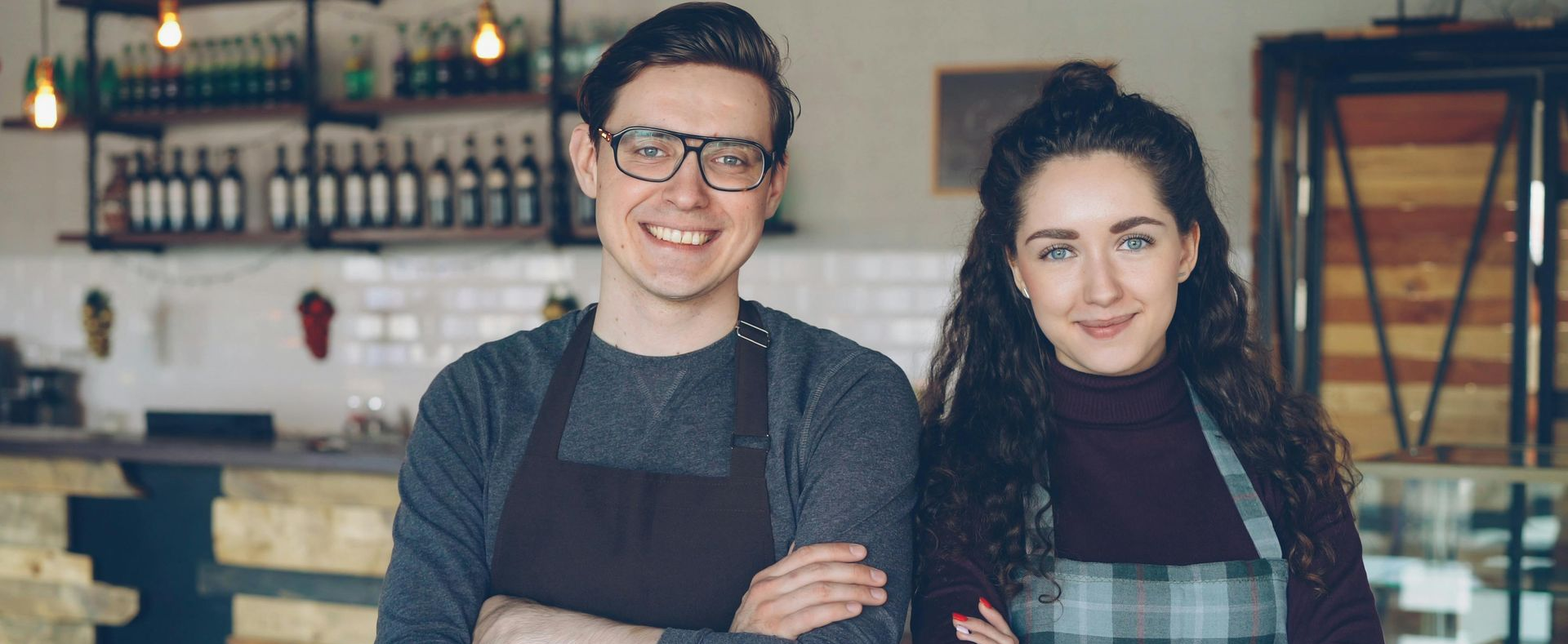 Two smiling café staff in aprons standing behind a counter in a rustic coffee shop