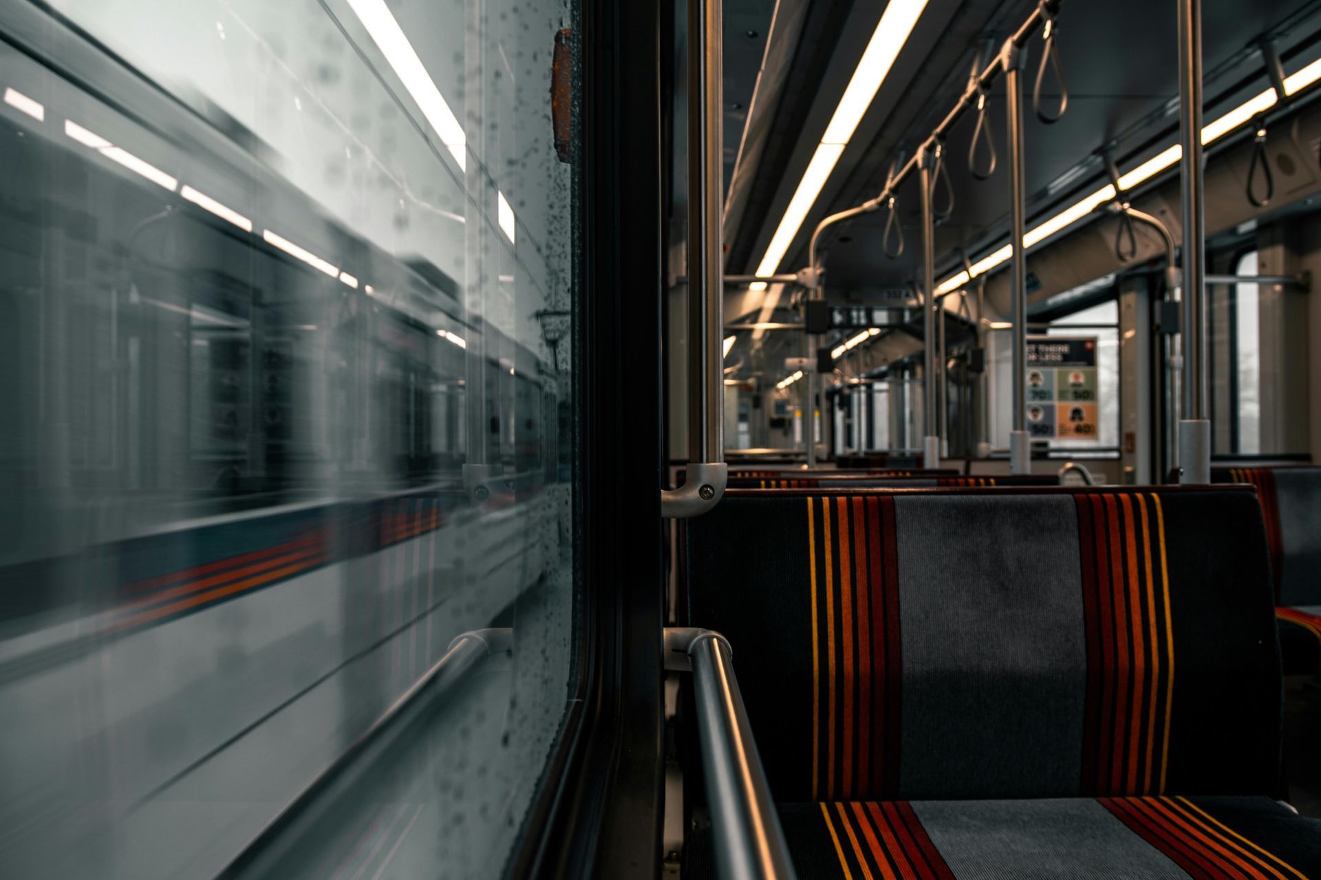 Empty train interior with striped seats beside a blurred train passing on the left