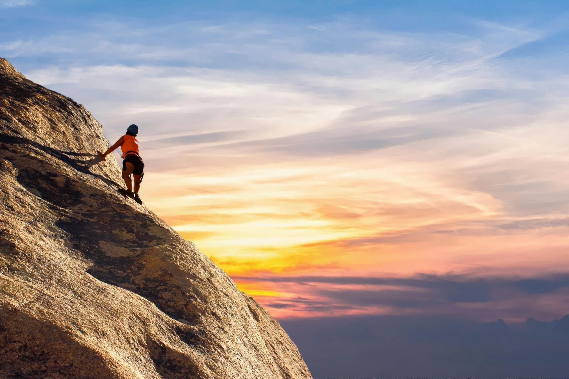 Climber standing on a rocky cliff at sunset with a glowing sky