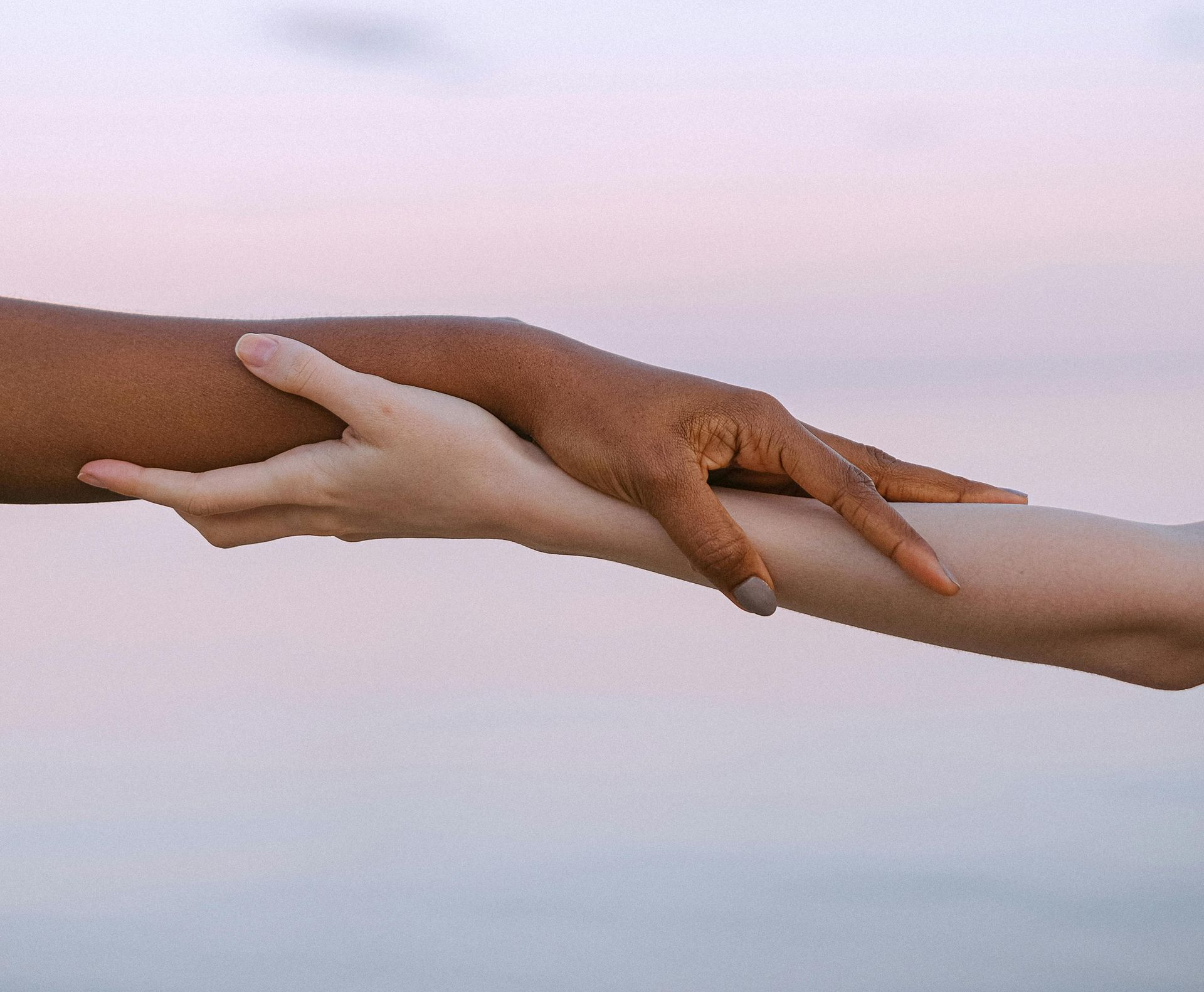 Two hands reaching toward each other against a soft pastel sky background