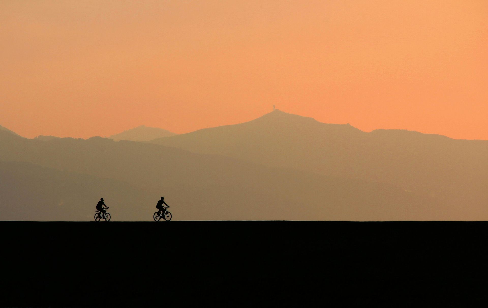 Two cyclists silhouetted against an orange sunset with mountains in the distance
