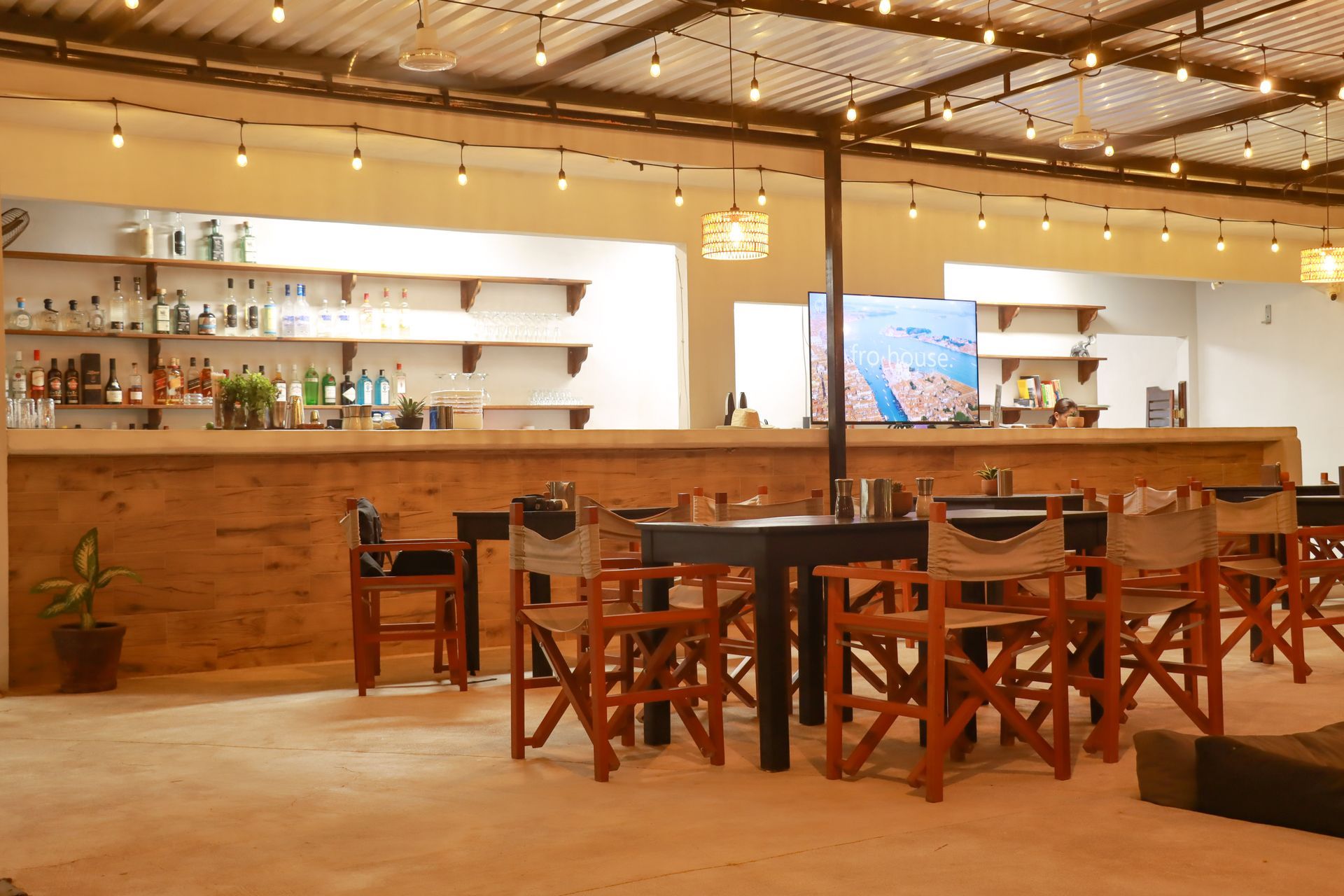 Bar moderno vacío con sillas de madera, estantes blancos e iluminación cálida.
