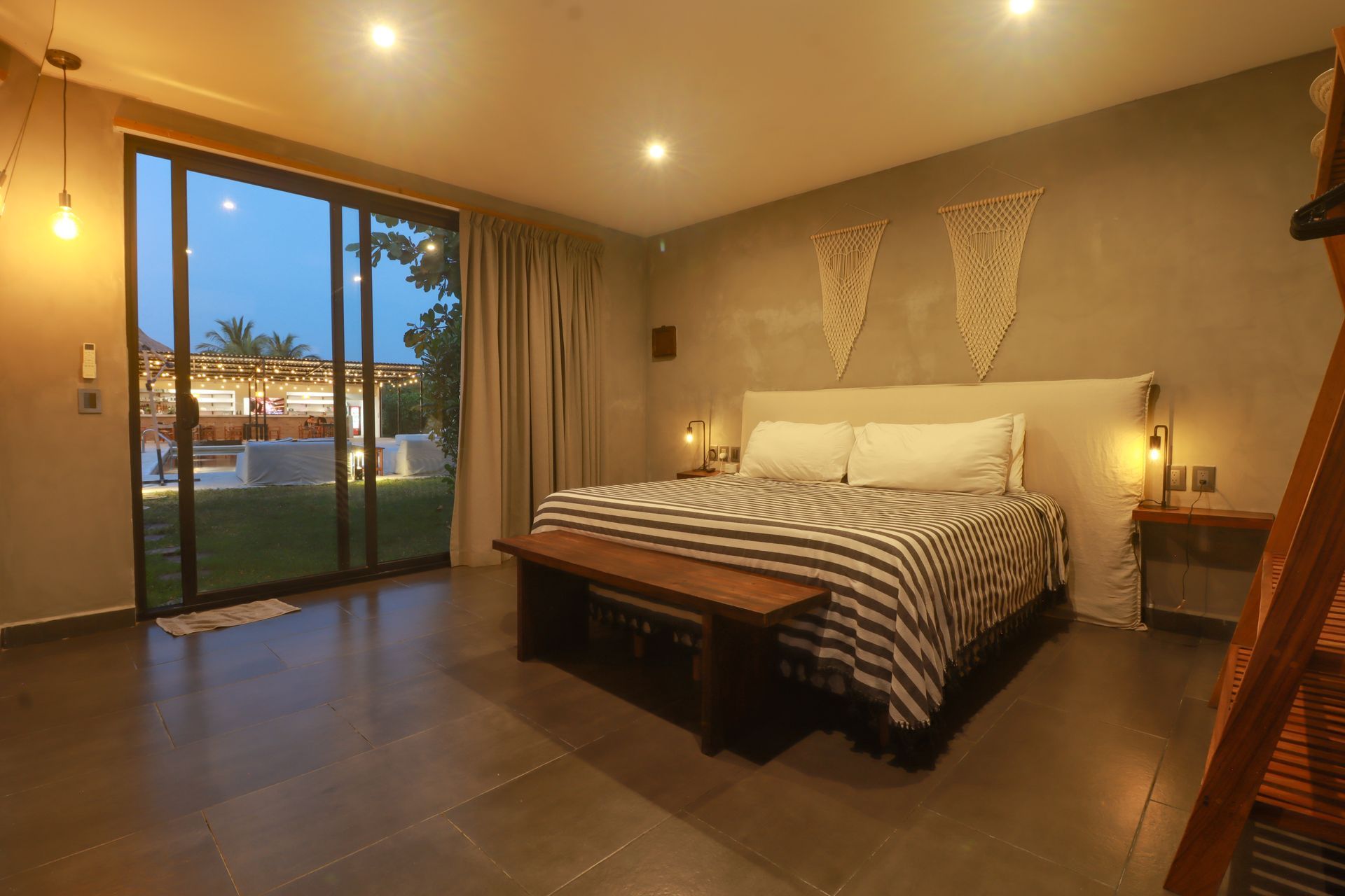 Habitación acogedora con una cama grande, iluminación cálida y puertas corredizas de vidrio que dan a un patio al atardecer.