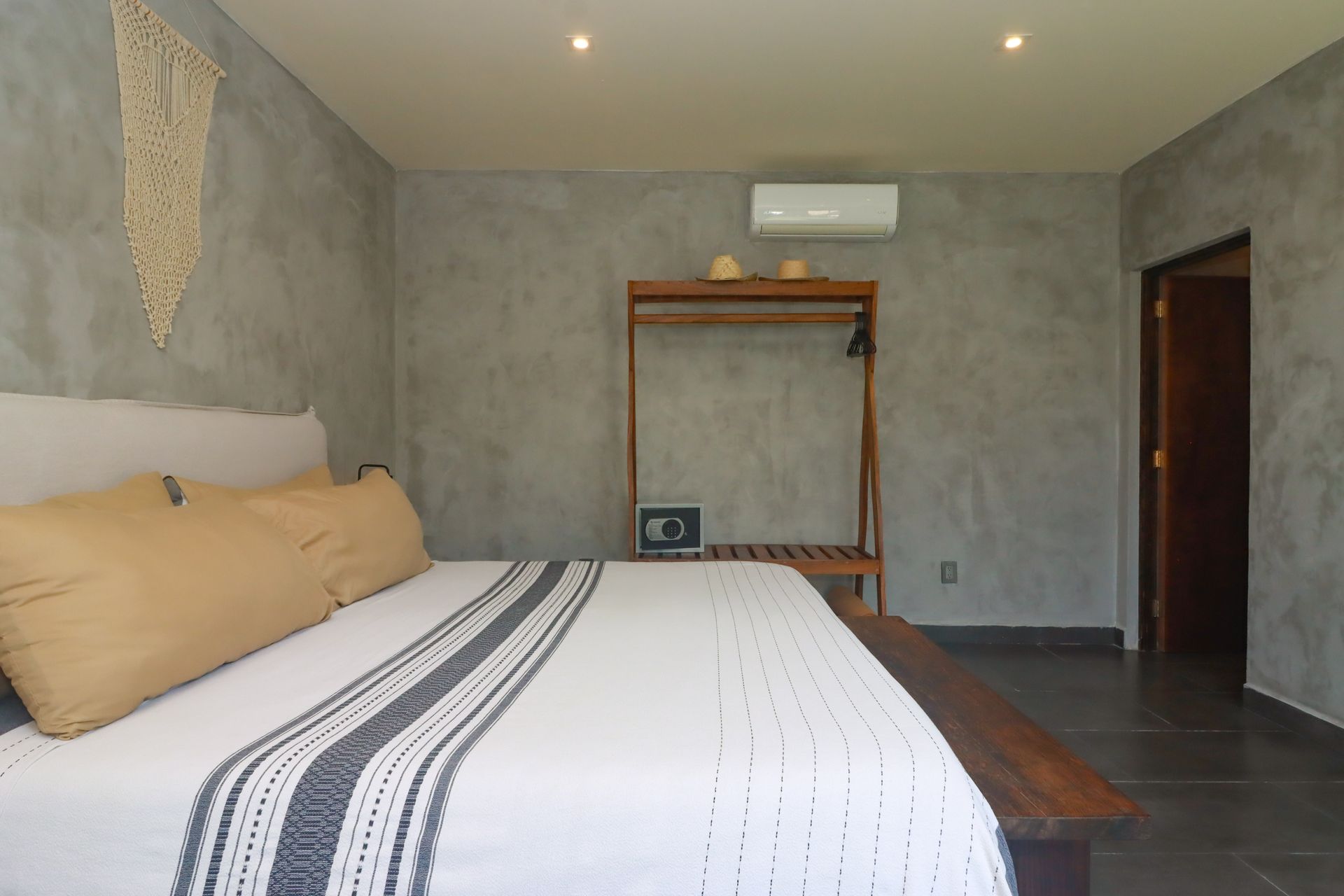 Dormitorio moderno con una cama grande, paredes de hormigón, estantería de madera y suelo de baldosas oscuras.