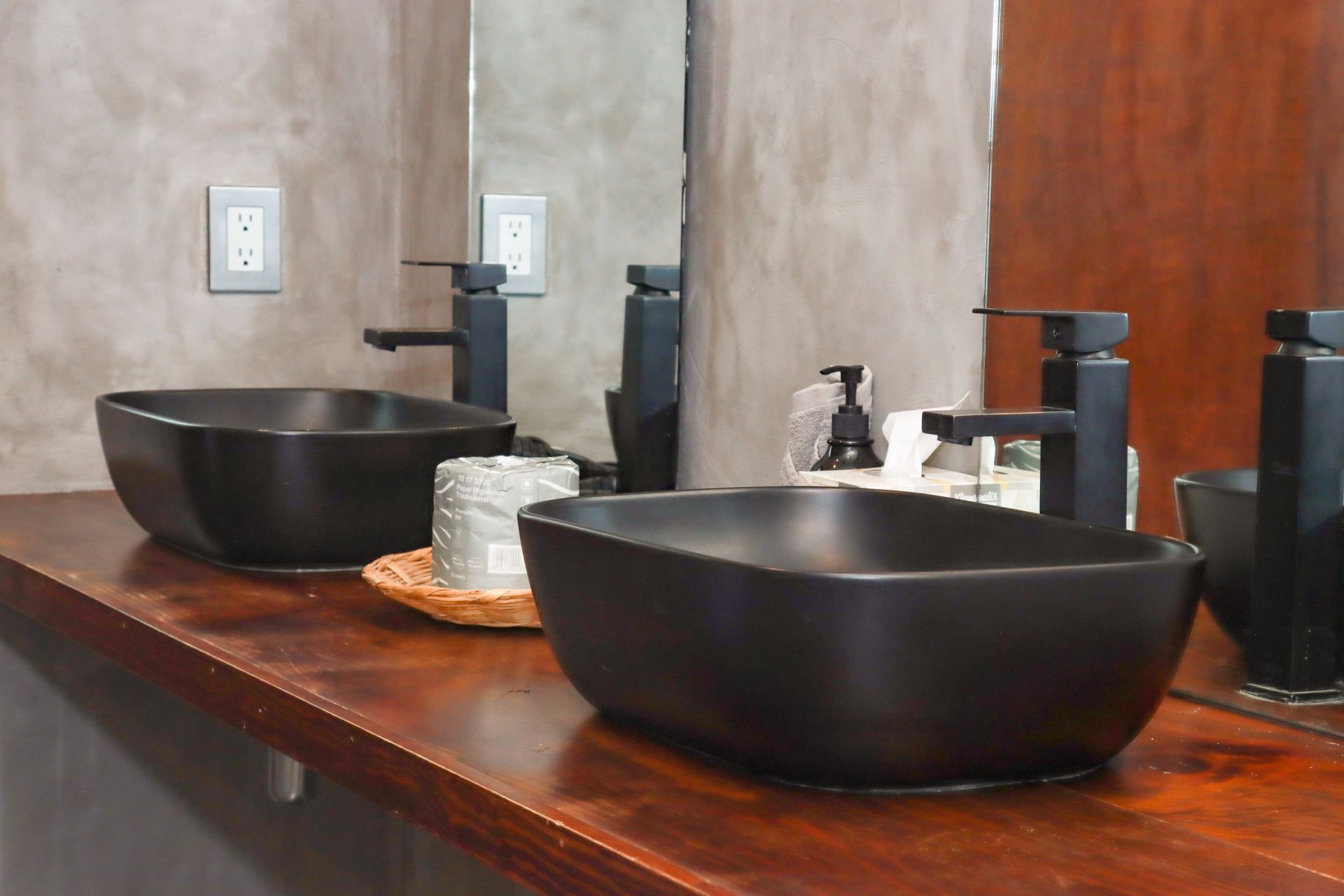 Lavabos negros sobre un mueble de baño de madera con espejos y grifos.