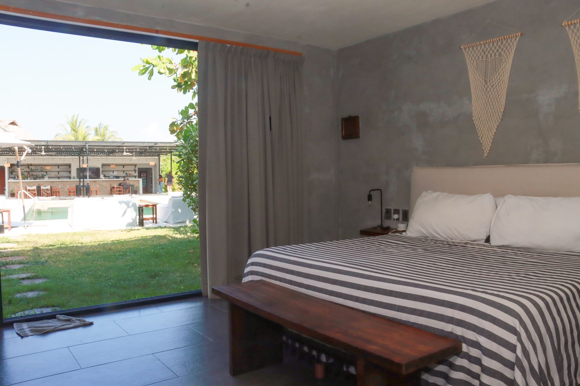 Dormitorio con colcha a rayas, puerta corredera abierta y vistas a un jardín con césped.