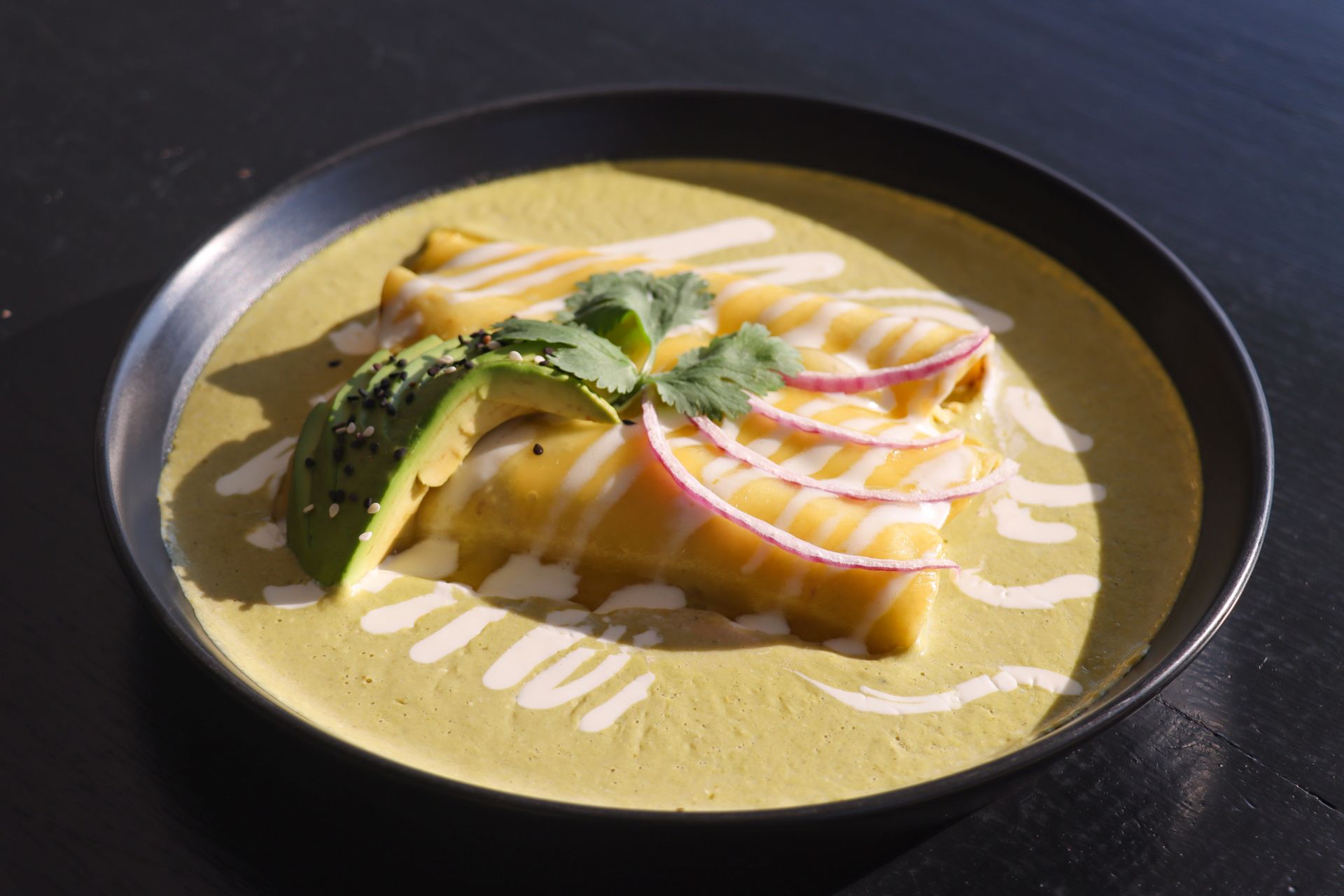 Curry amarillo emplatado con aguacate, hierbas y fruta en rodajas sobre una mesa oscura.