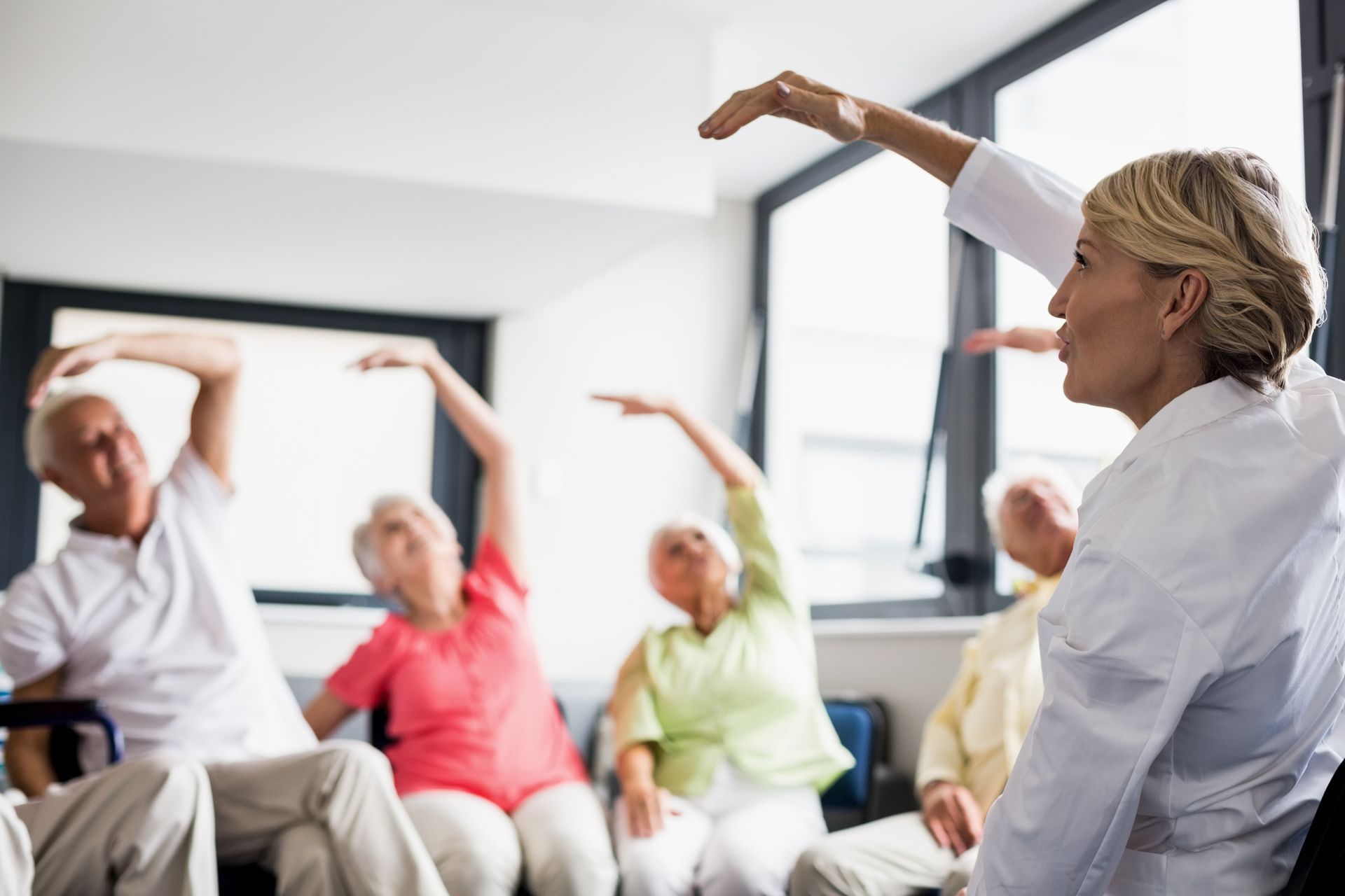 People doing physical therapy exercises in a bright rehab gym, with one standing at a table and others using exercise equipment. People doing physical therapy exercises in a bright rehab gym, with one standing at a table and others using exercise equipment.