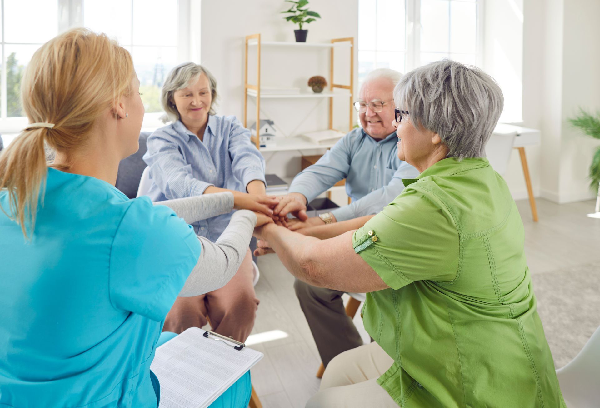 People sitting in a circle, holding hands during a group support meeting in a bright room