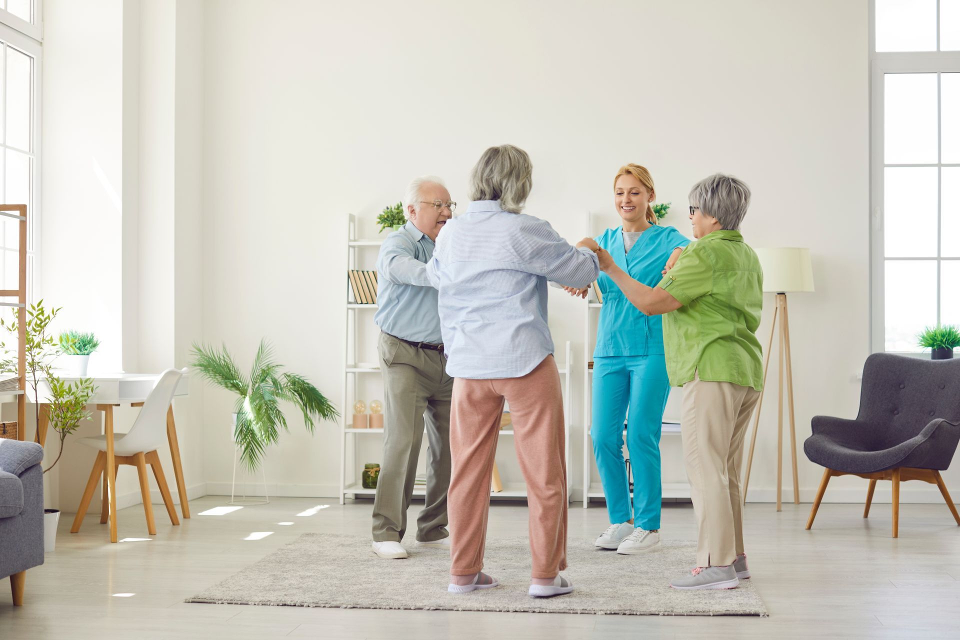 Four people holding hands in a bright living room, smiling in a circle during a group activity
