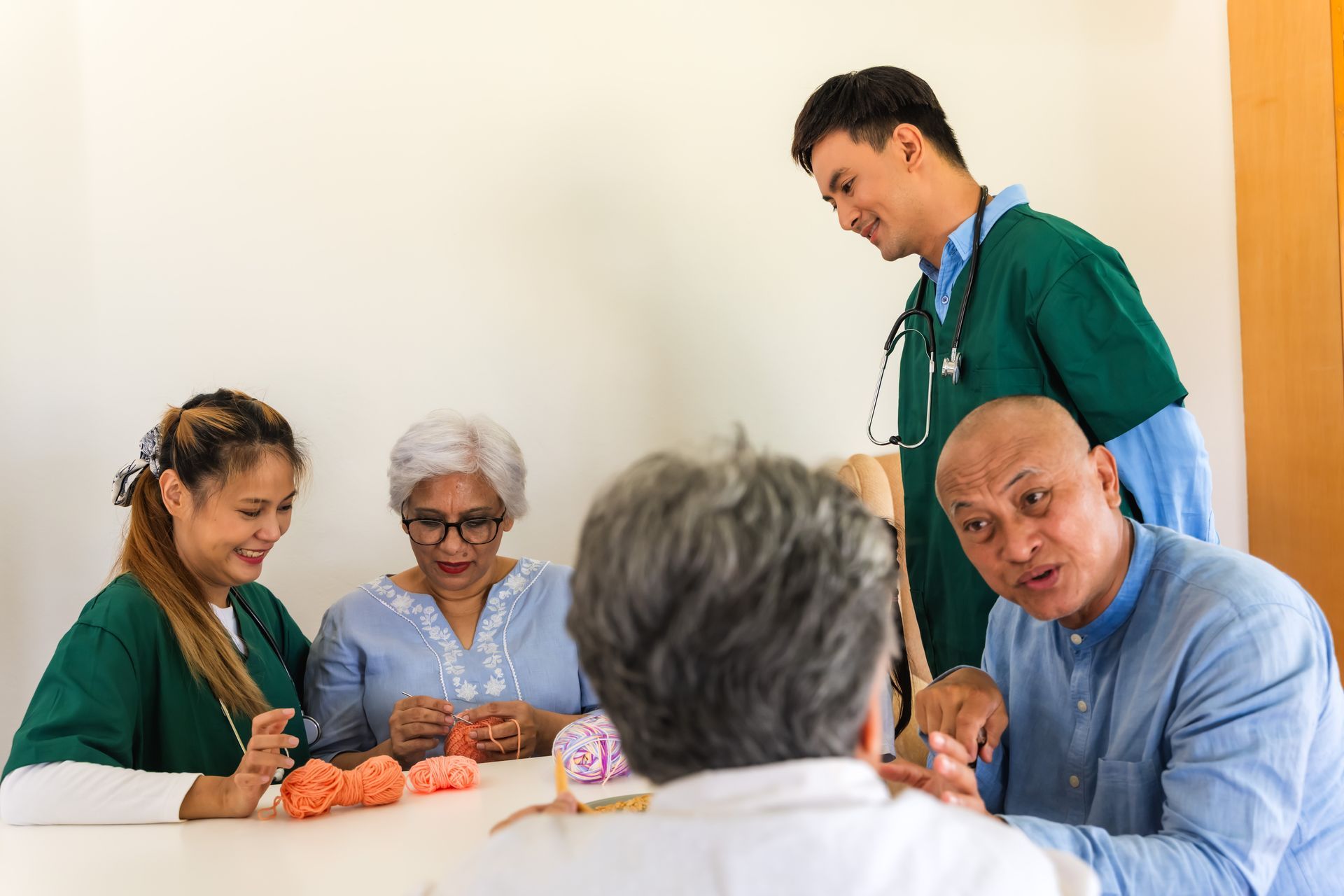 People in scrubs and a seated man gather around a table with medical models in a clinic setting People in scrubs and a seated man gather around a table with medical models in a clinic setting