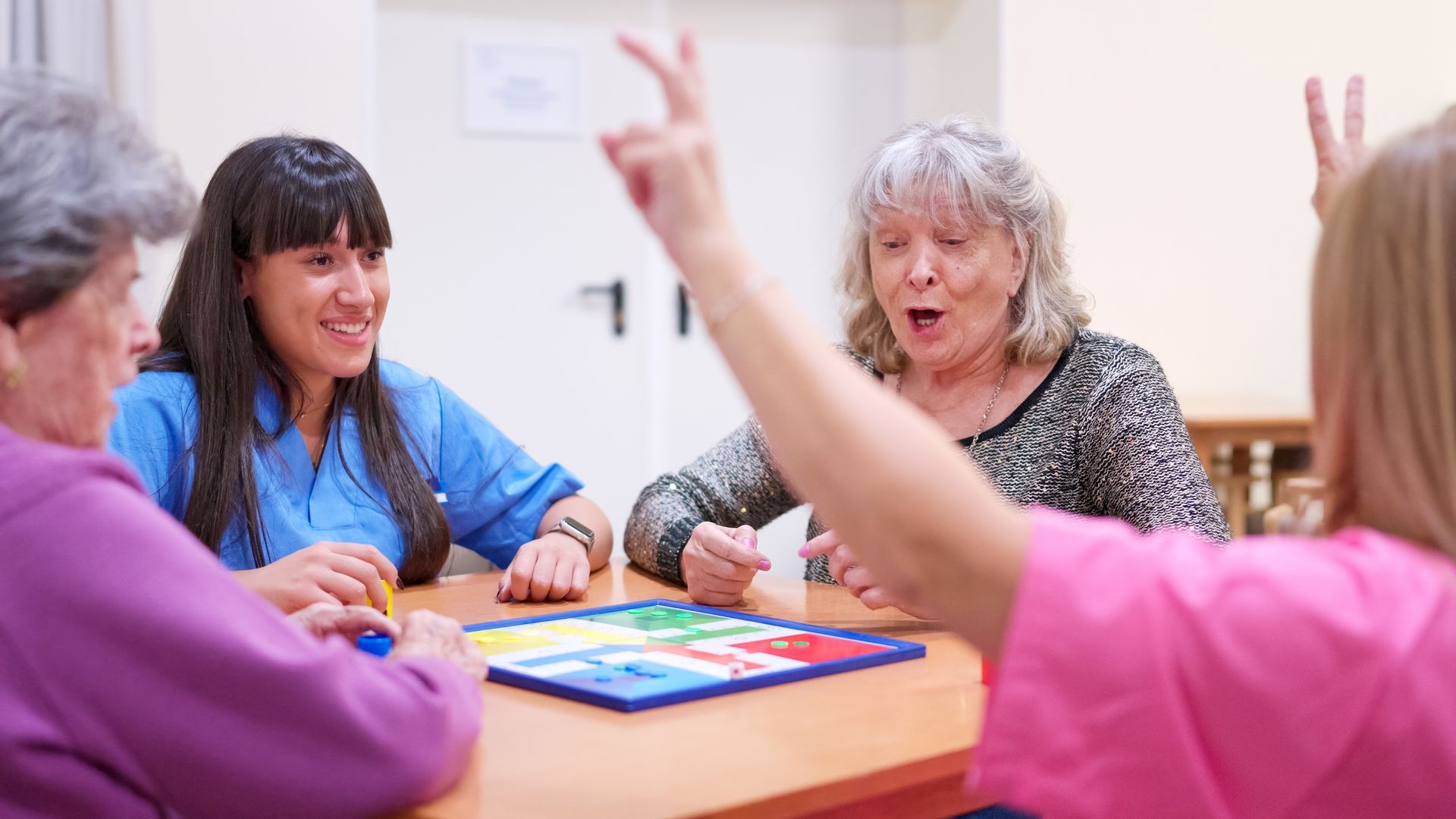 People seated at a table in a bright classroom, talking and gesturing during a group activity People seated at a table in a bright classroom, talking and gesturing during a group activity