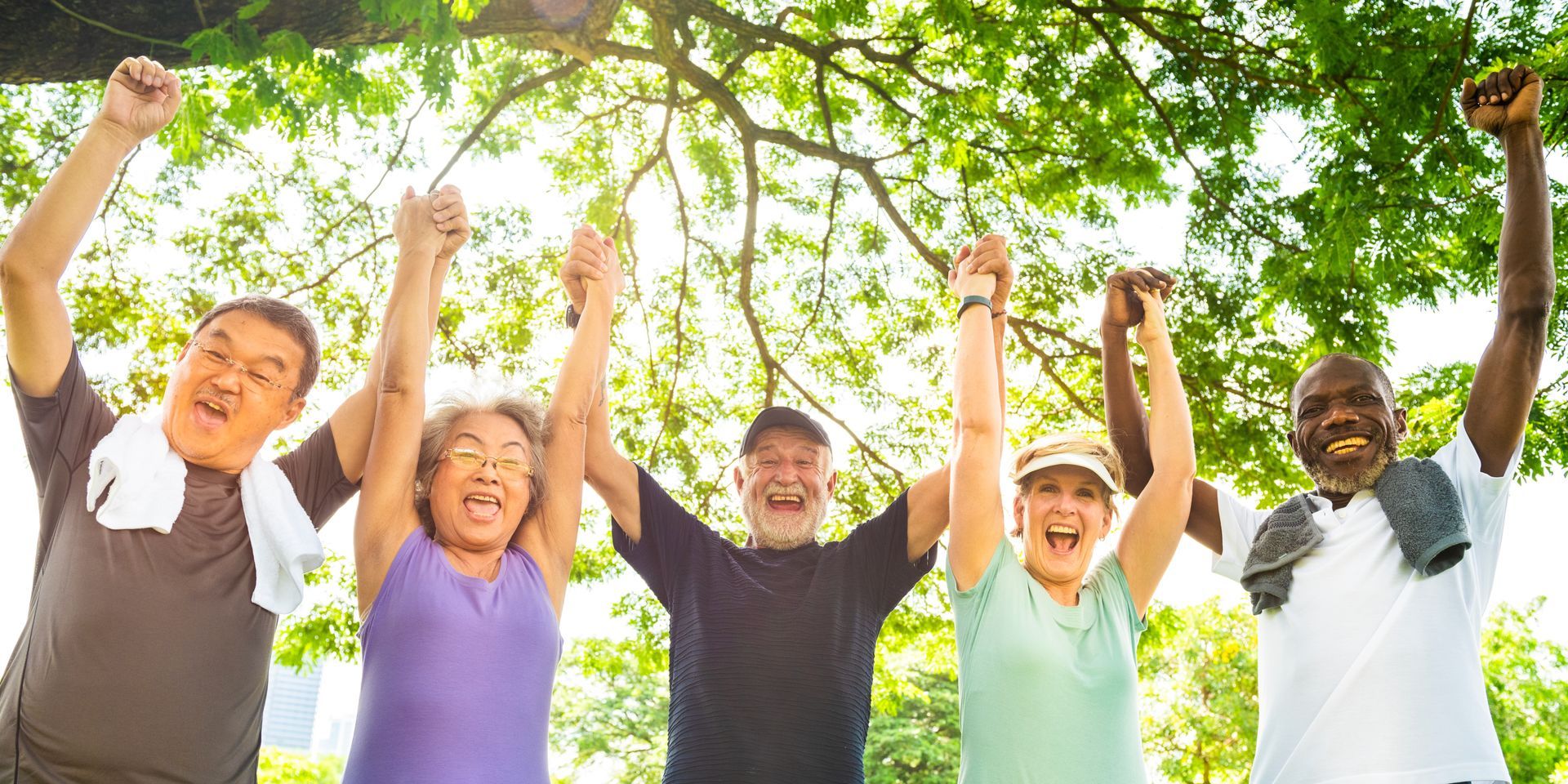 A group of people cheering with raised arms under green trees outdoors A group of people cheering with raised arms under green trees outdoors