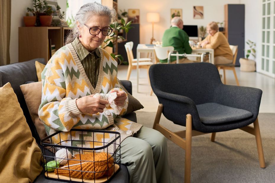 Person knitting in a bright living room with a basket of yarn beside them