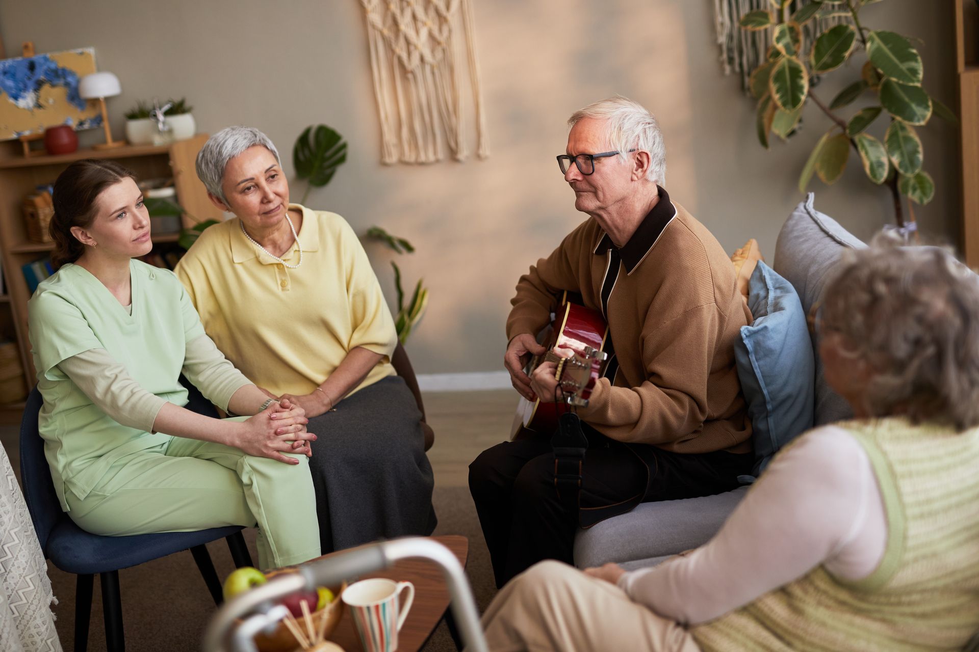 Small group in a living room talking while one person plays guitar.