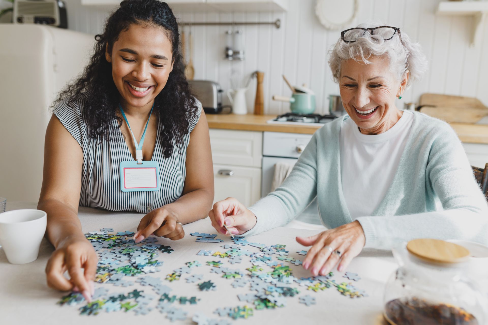 Two women smiling while assembling a jigsaw puzzle at a kitchen table